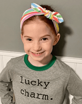 Girl is wearing a handmade knot headband featuring a rainbow print from By Bella Boutique.